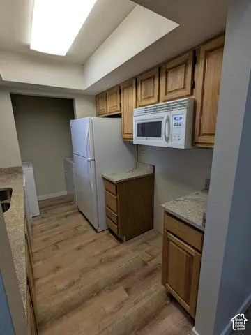 Wood-finish flooring with light-toned cabinetry, granite-style countertops, and an integrated overhead microwave