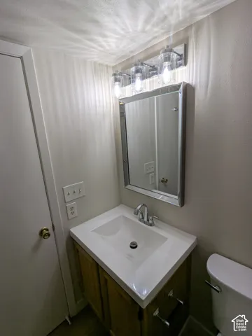 Vanity with a white integrated sink and chrome faucet, wood-finish cabinetry, framed mirror, and three-bulb vanity lighting