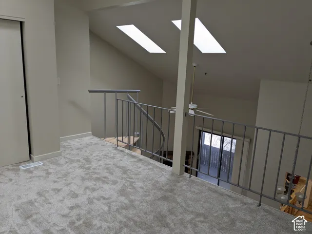 Carpeted loft space with a vaulted ceiling, two skylights, and a ceiling fan