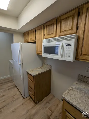 Wood-finish flooring with oak cabinetry, stone-finish countertops, and built-in microwave