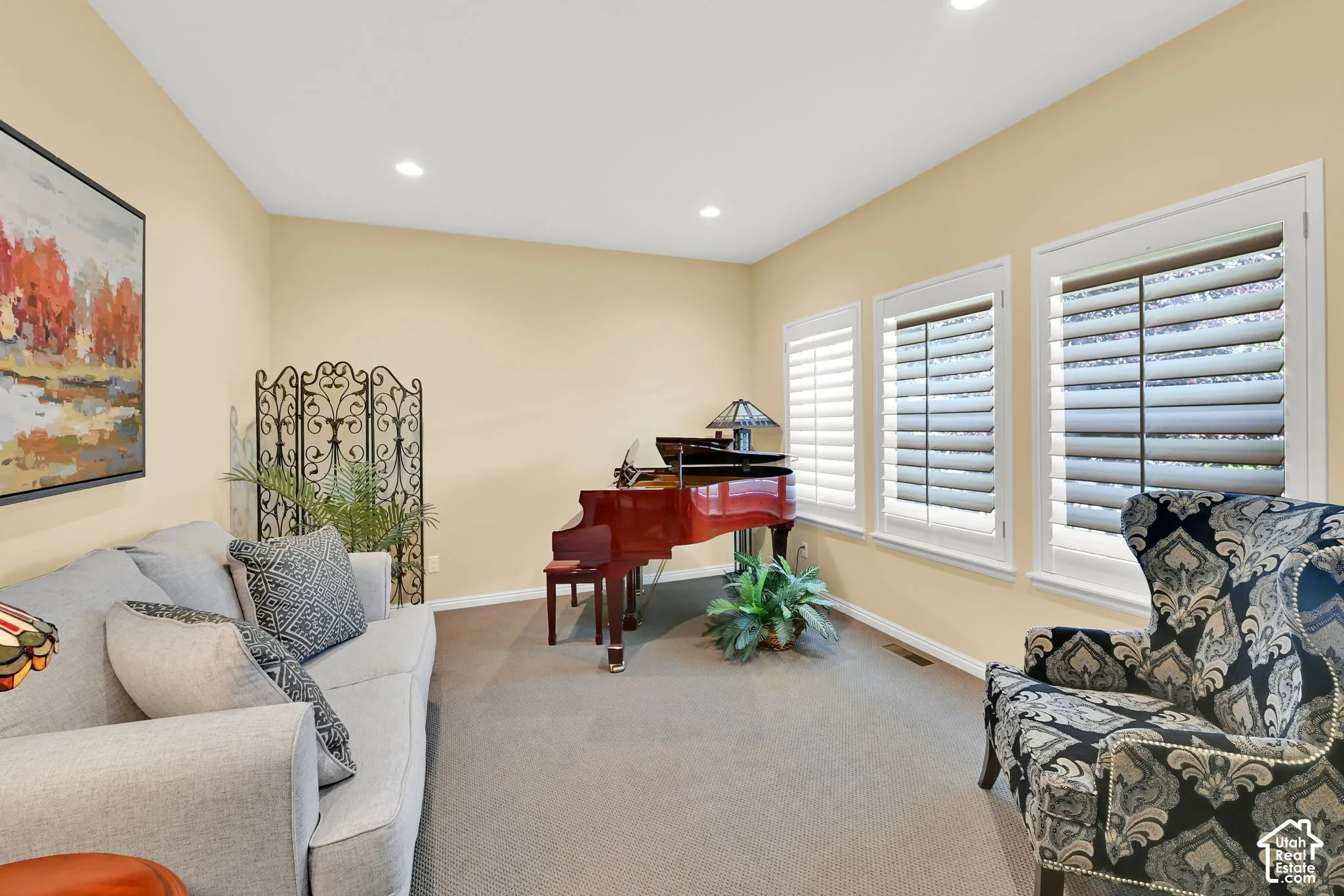 Recessed ceiling lighting, three windows with plantation shutters, neutral-toned carpeting, and light-colored walls