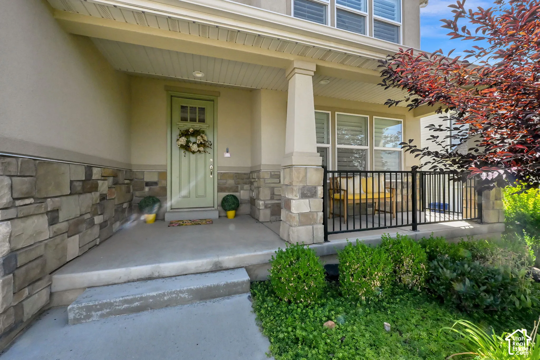 Covered front porch with stone accents, a light green entry door, and multi-pane windows