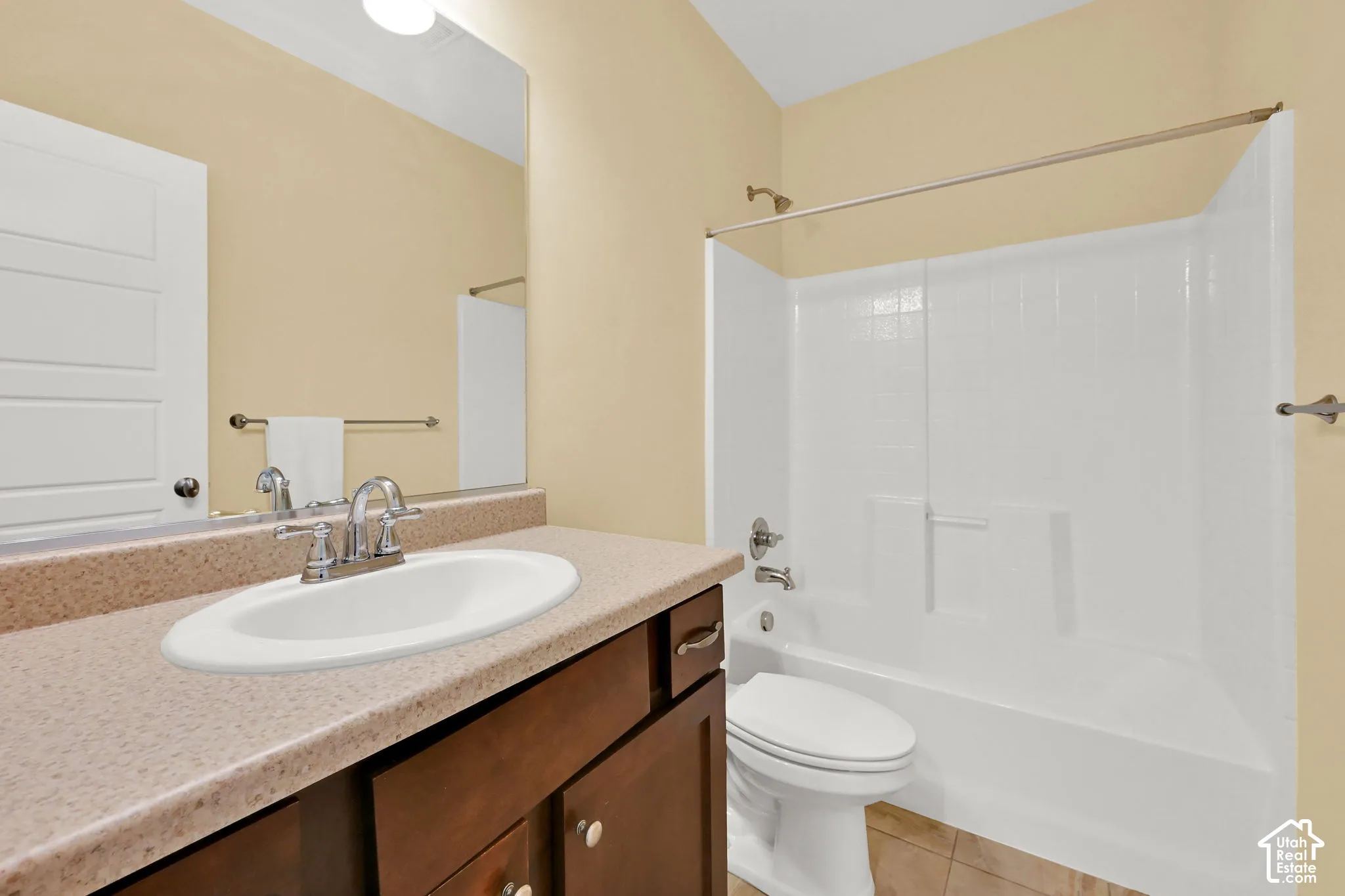 Bathroom featuring a single vanity with a speckled countertop, an integrated oval sink, a wall-mounted mirror, and a white bathtub with a shower