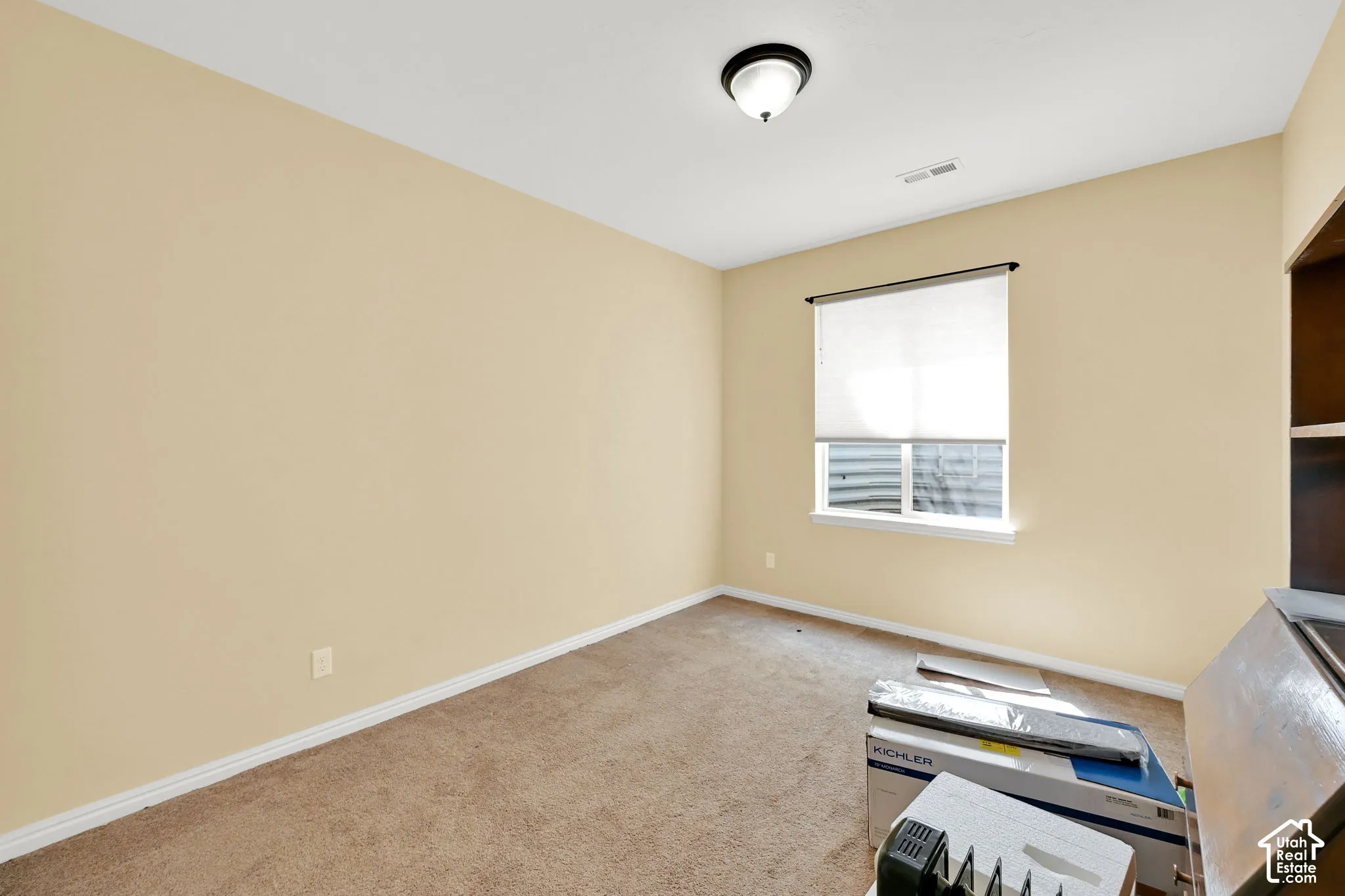 Carpeted room with a single window featuring a roller shade