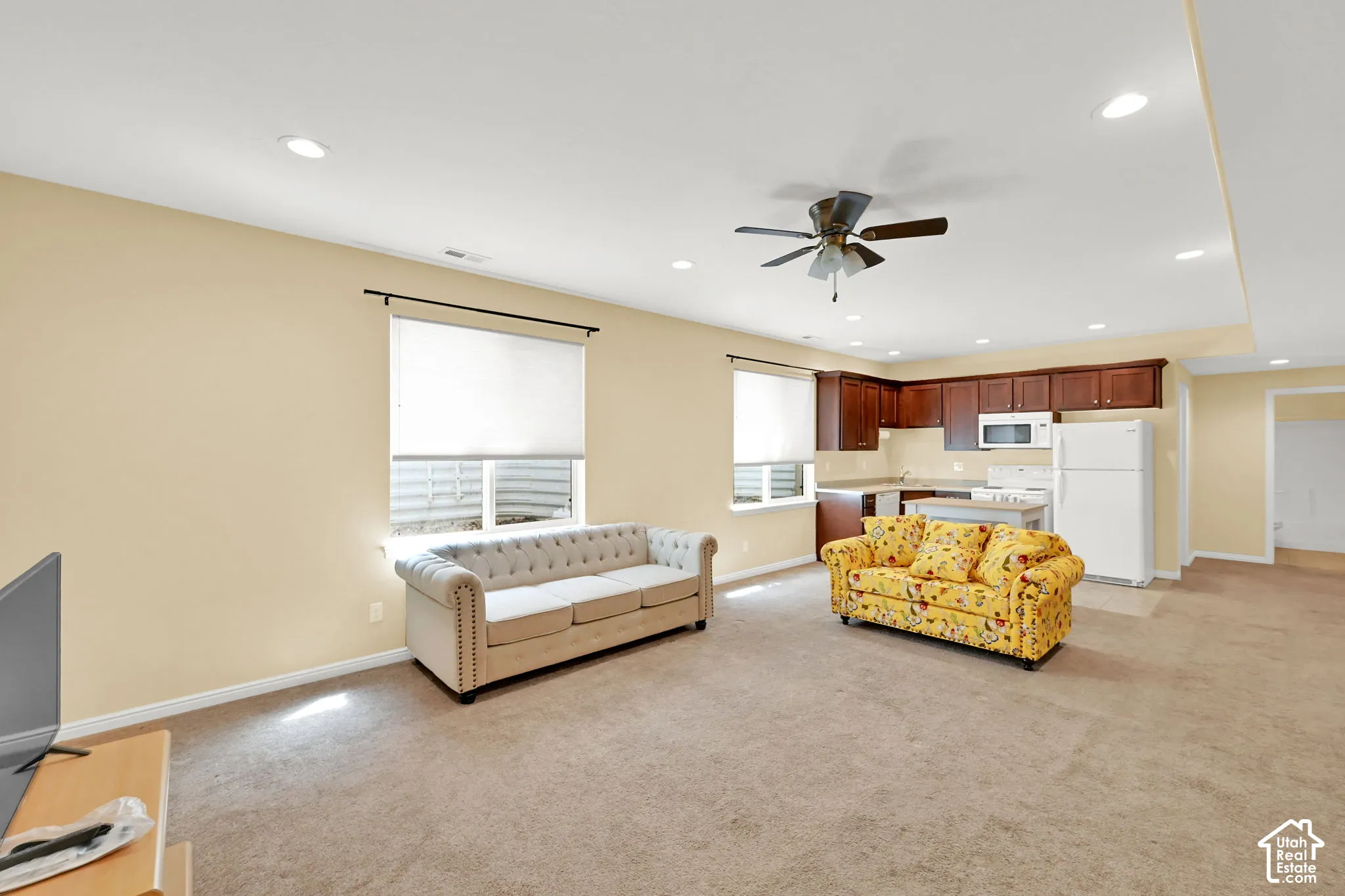 Recessed ceiling lighting, ceiling fan, carpet flooring, full kitchen with wood cabinetry and white appliances, and window with privacy blind