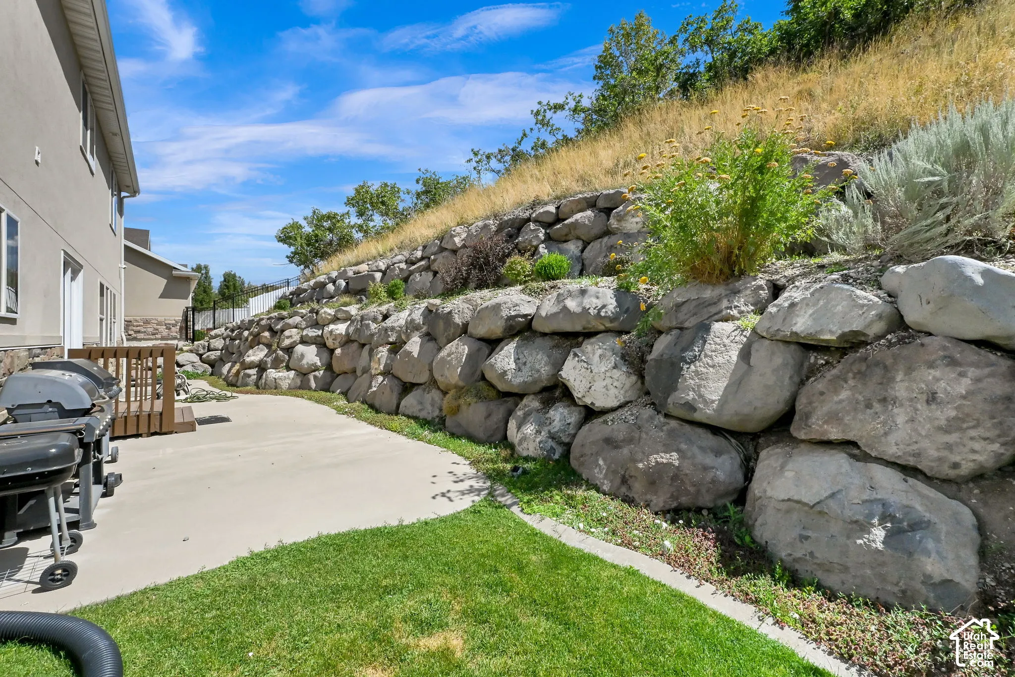 Stucco exterior with stone accenting, concrete patio, and a multi-level retaining wall