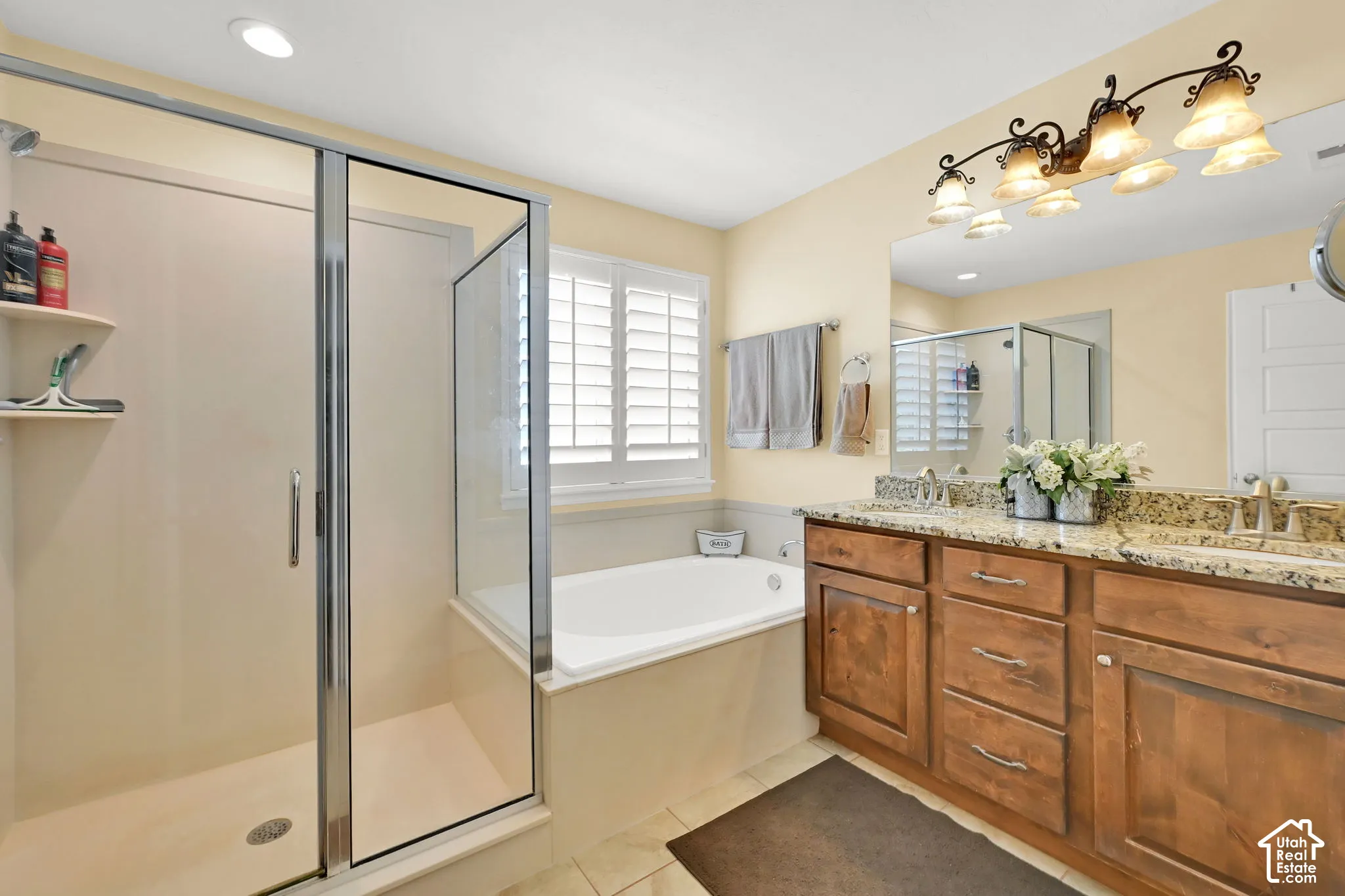 Walk-in shower with glass enclosure, separate soaking tub, dual vanity with granite countertop, and wood-finish cabinetry