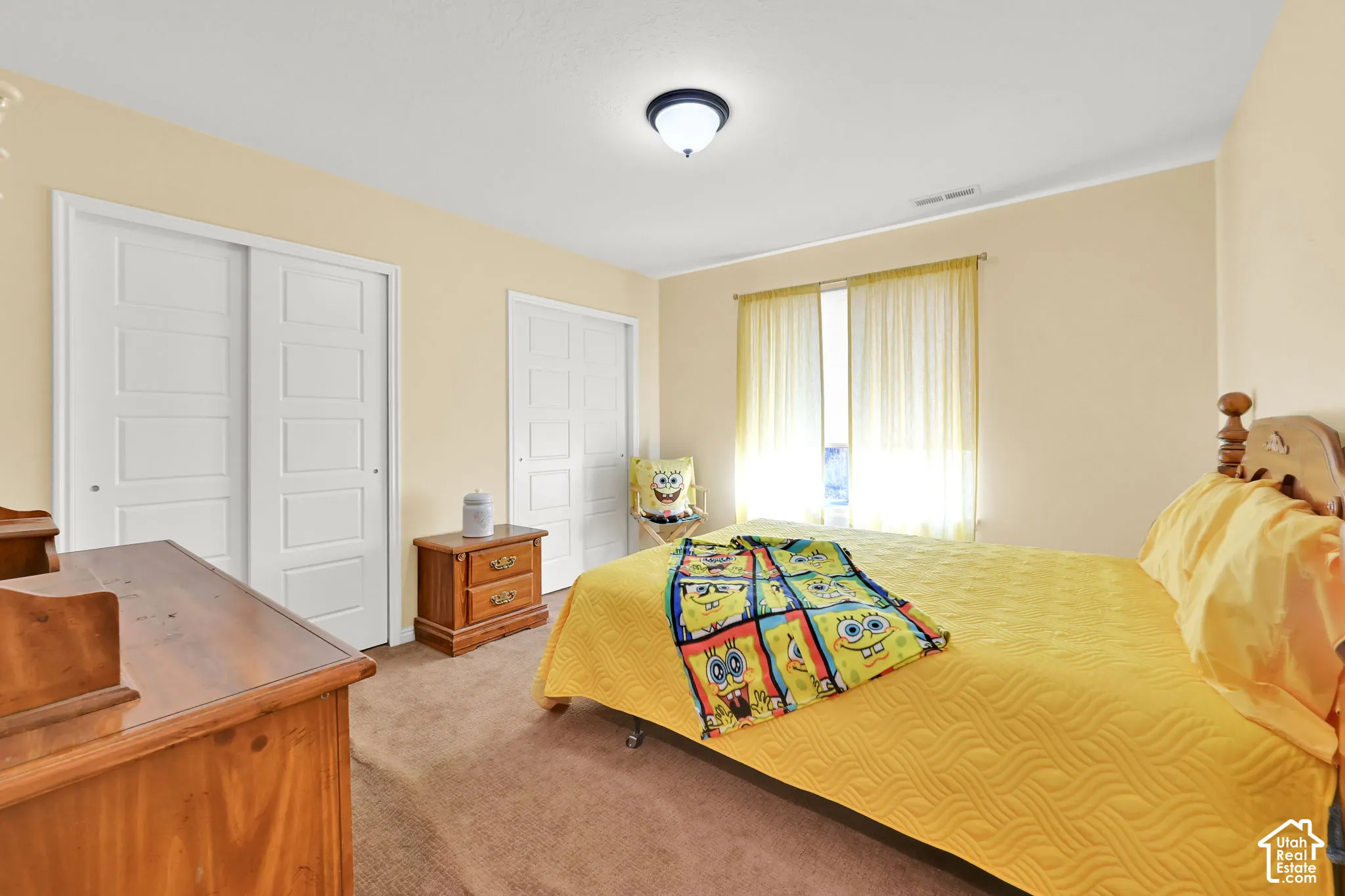 Recessed ceiling light, two white sliding panel closets, neutral carpeting, and a window with sheer coverings