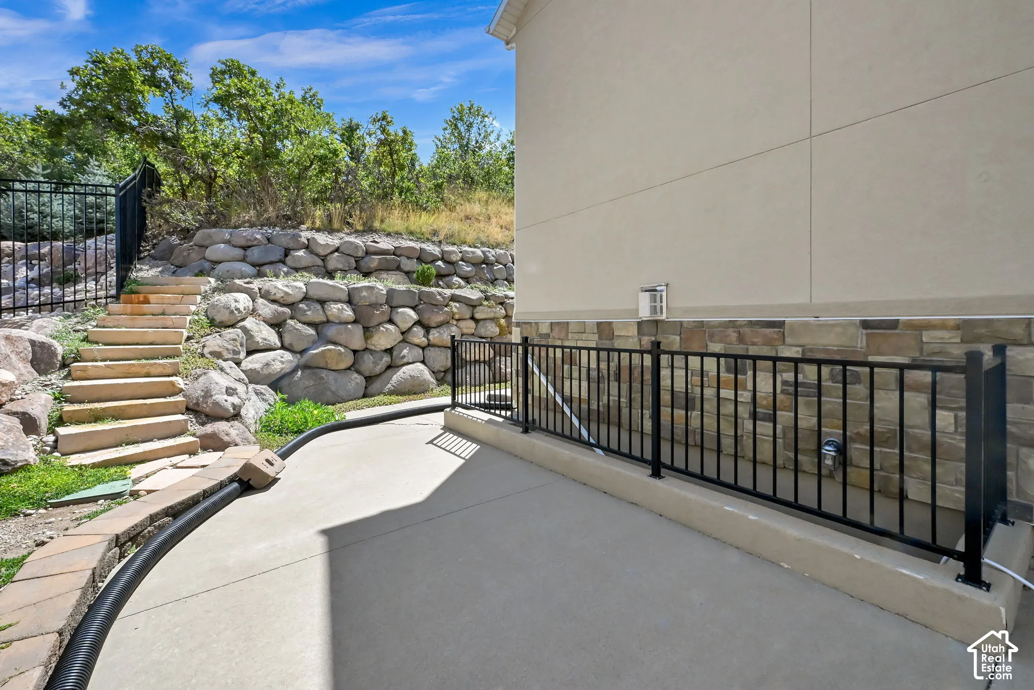 Concrete patio featuring a stone veneer foundation, stucco siding, and black metal railings
