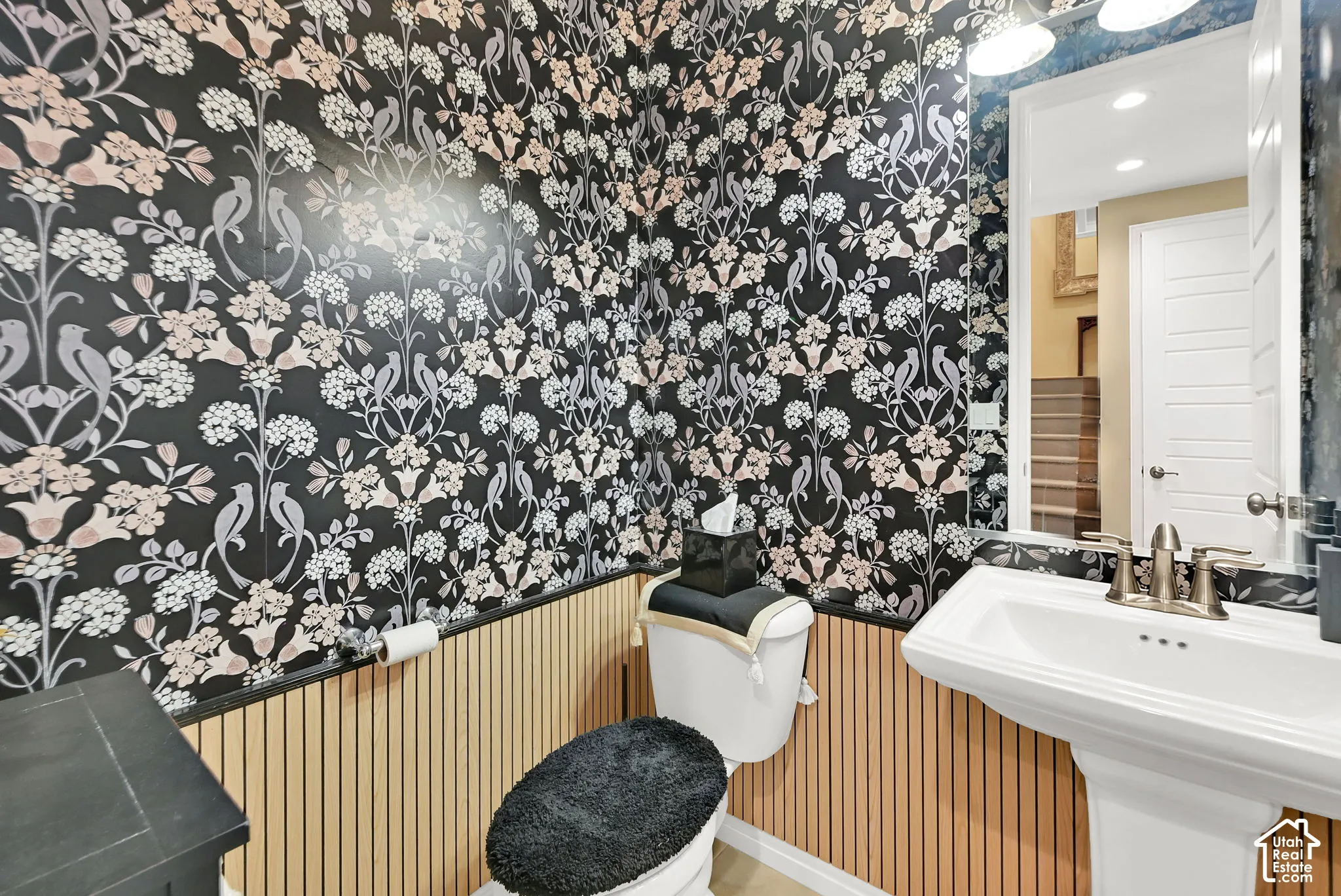 Pedestal sink with a brushed nickel faucet, full vanity mirror, and decorative wall paneling
