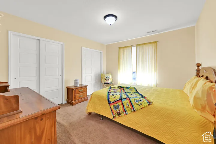 Recessed ceiling light, two white sliding panel closets, neutral carpeting, and a window with sheer coverings