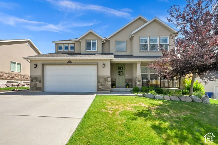 Stucco exterior with stone veneer accents, covered front entry, attached garage, and established landscaping