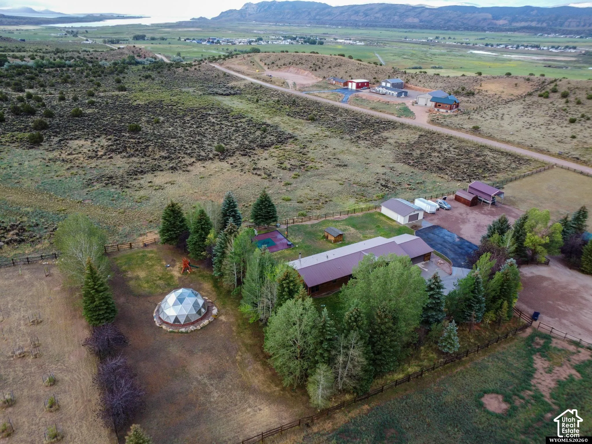 Expansive property featuring a geodesic dome, multiple outbuildings, fenced perimeter, mature trees, and a paved driveway