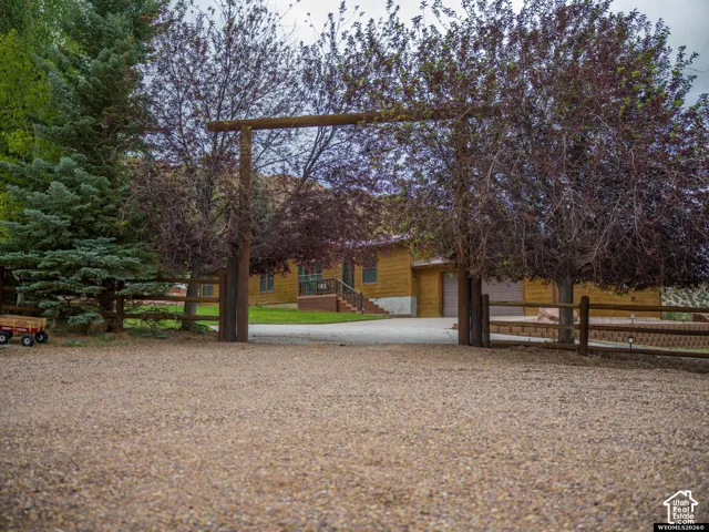 Gravel driveway with a wood-beam entryway, leading to a wood-sided residence