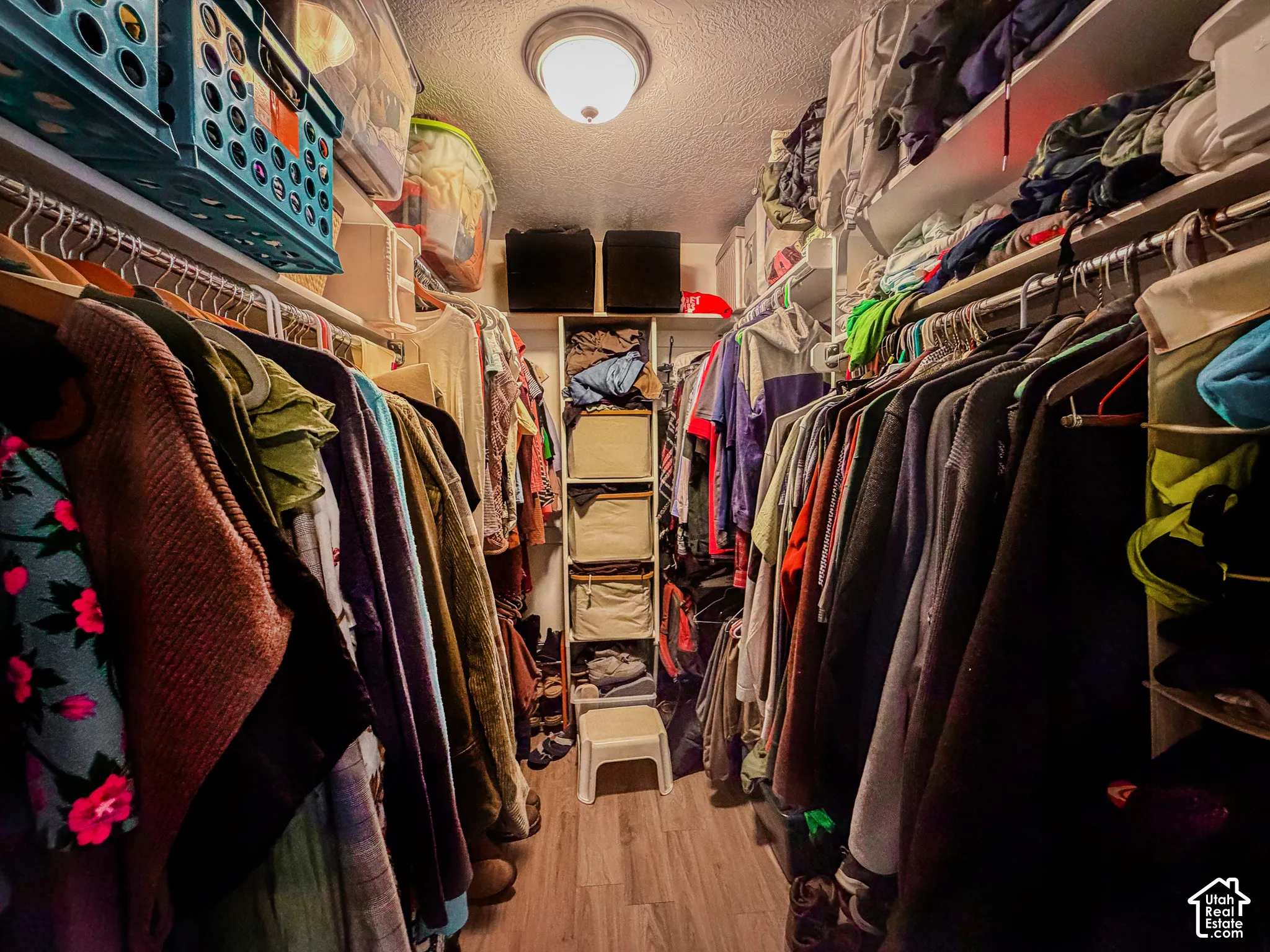 Recessed ceiling light fixture illuminates this walk-in closet featuring built-in shelving, multiple hanging rods, and wood-finish flooring