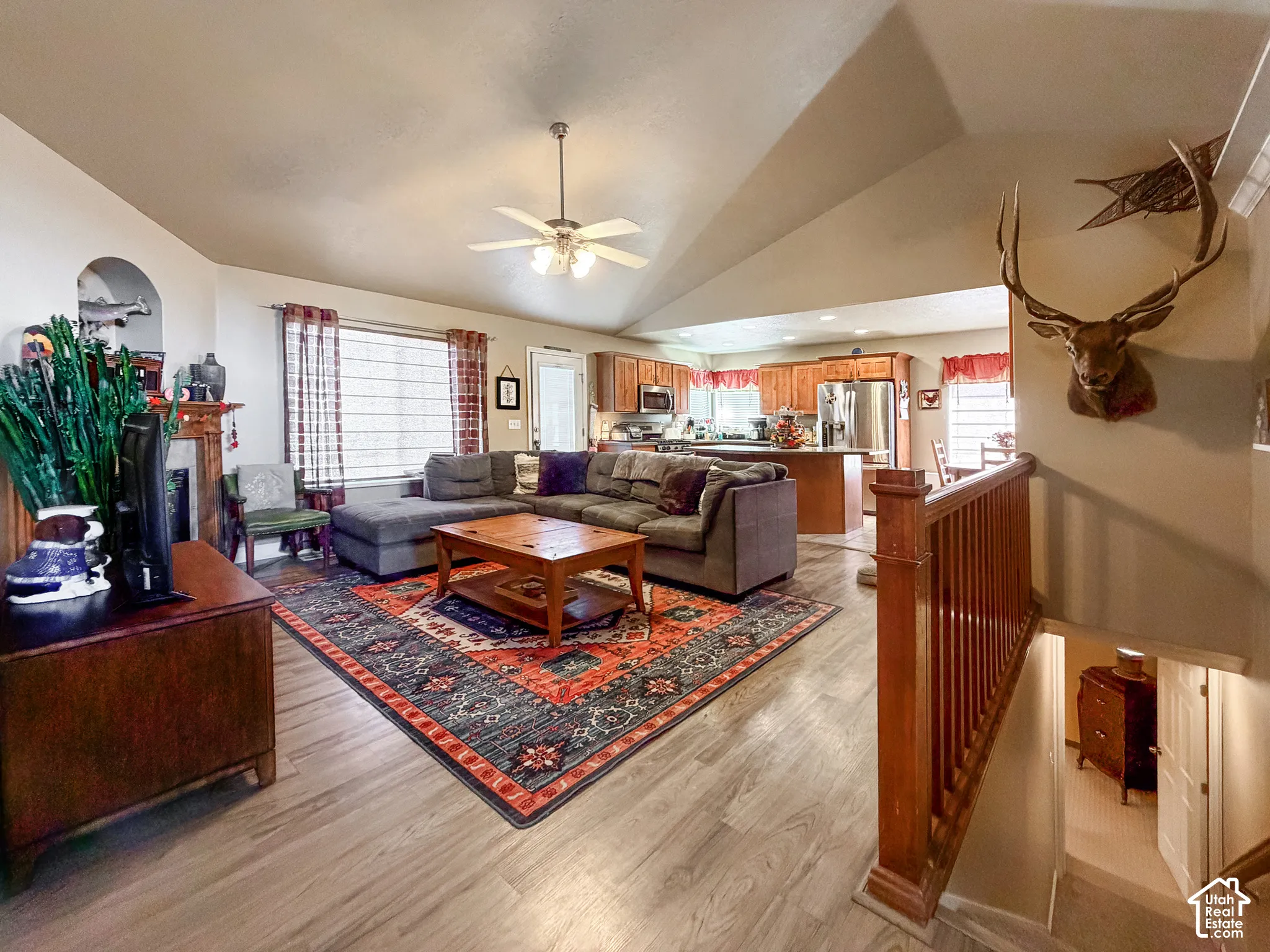 Vaulted ceiling with a ceiling fan, wood-finish flooring, wood cabinetry, stainless steel appliances, and a wood staircase