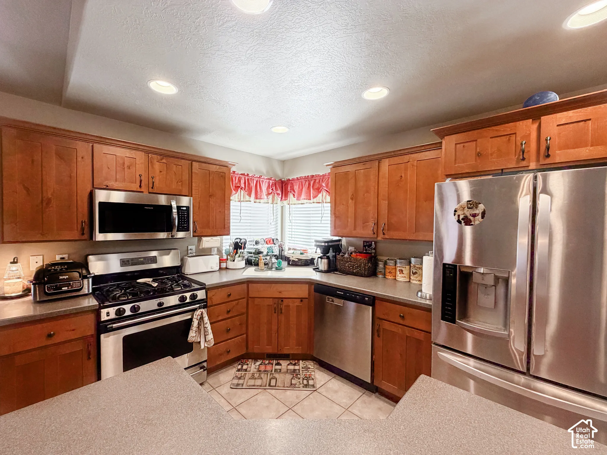 U-shaped kitchen with recessed lighting, wood-finish cabinetry, stainless steel appliances, and a tile floor