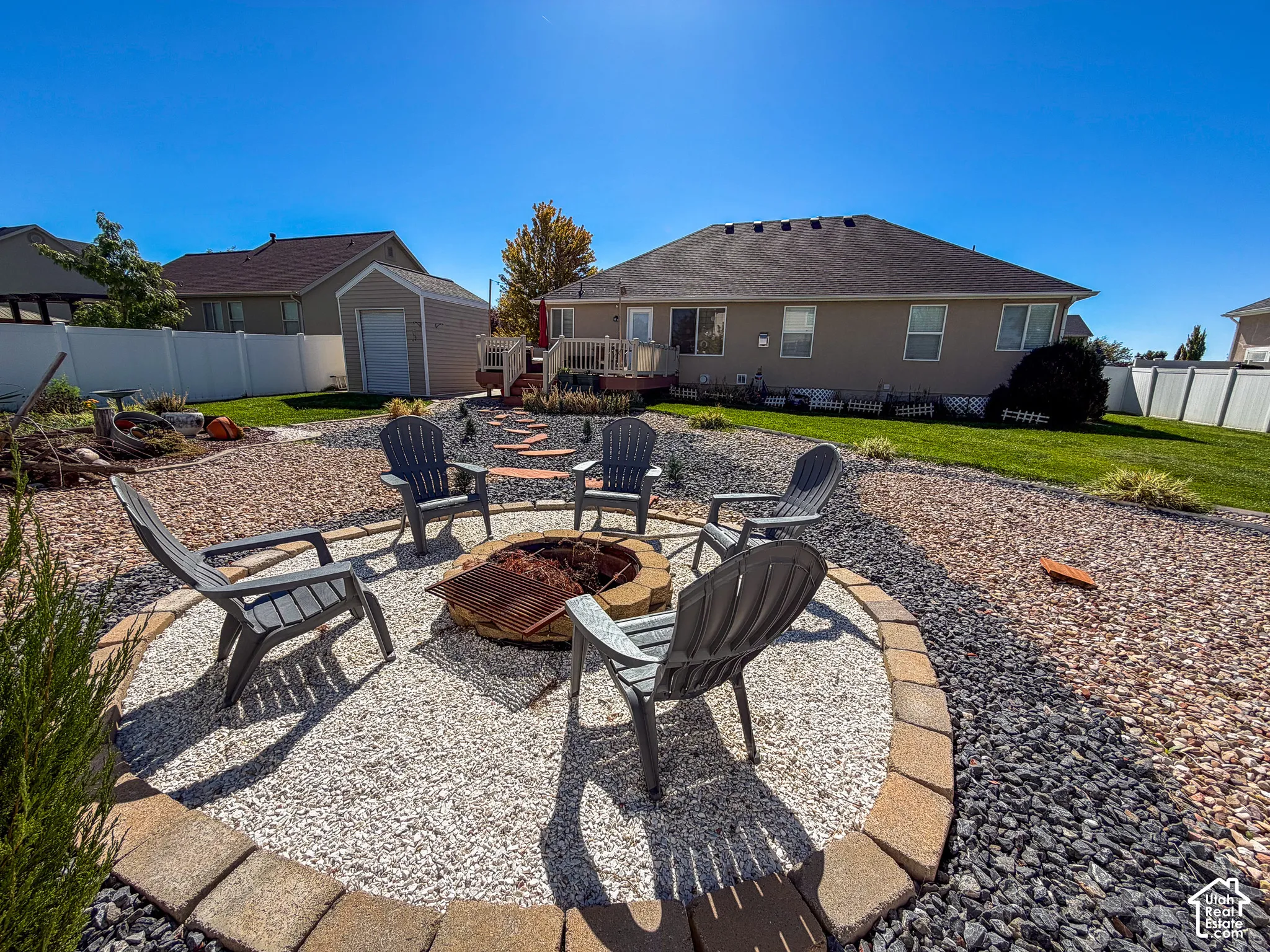 Backyard with a stone-edged fire pit area, gravel and rock landscaping, manicured lawn, and a shed structure