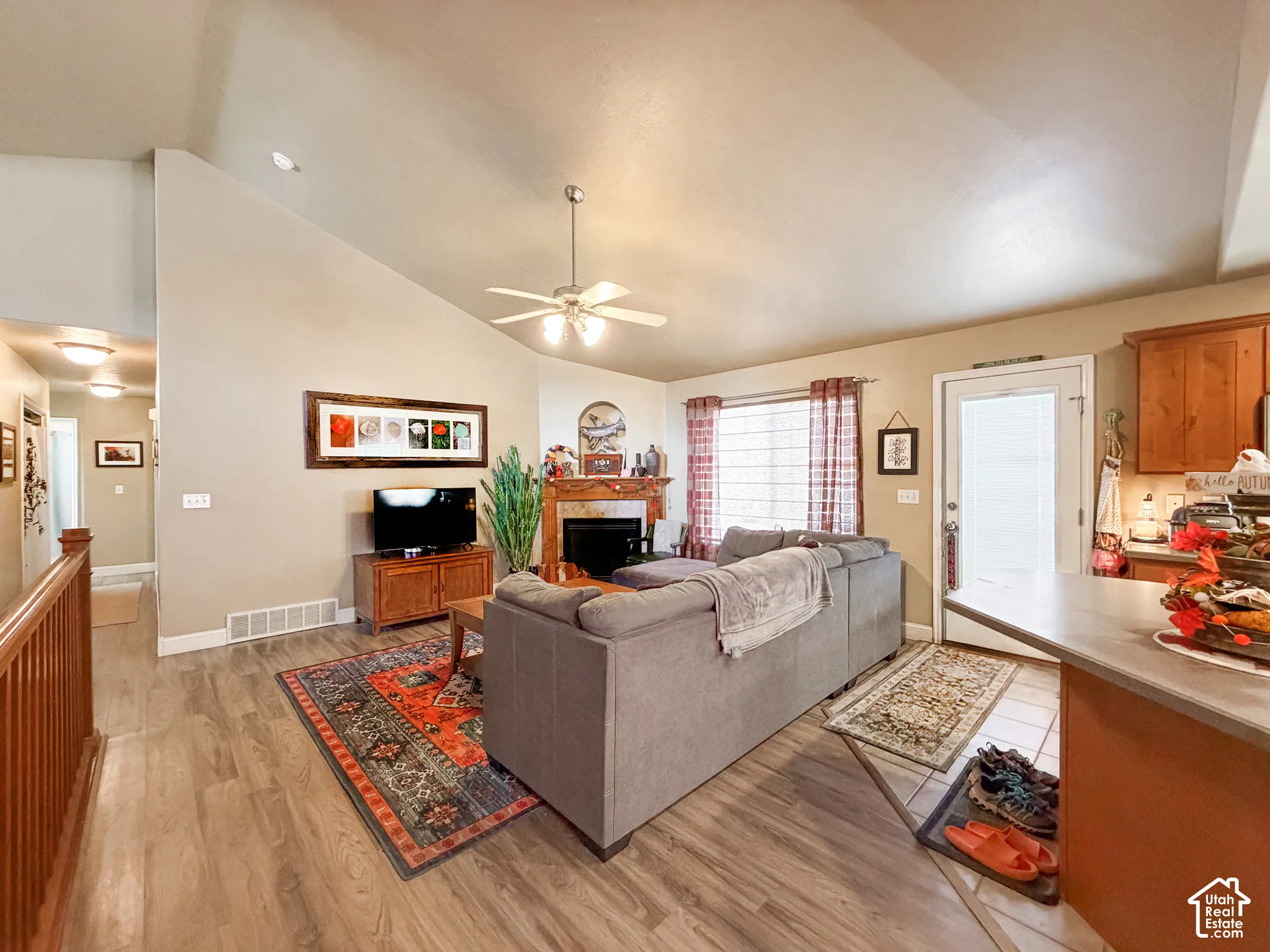 Vaulted ceiling with a ceiling fan, wood-finish flooring, fireplace with a wood mantle, wood cabinetry, and a countertop with an overhang