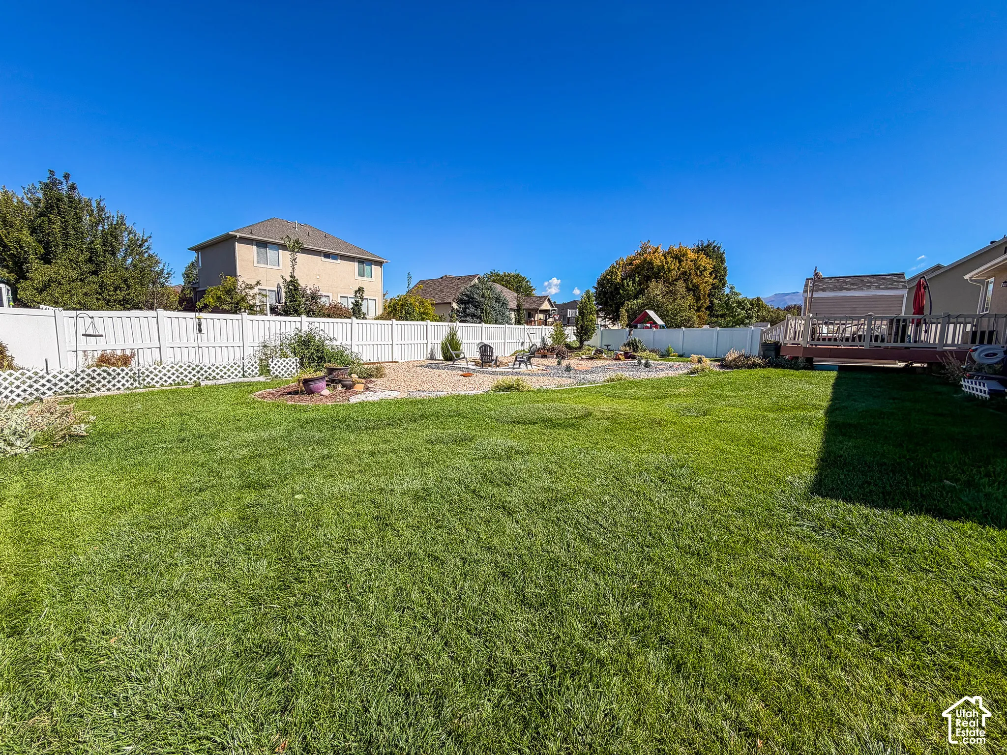 Expansive backyard featuring a lush lawn, white privacy fencing, a gravel landscaping area, and a wood deck