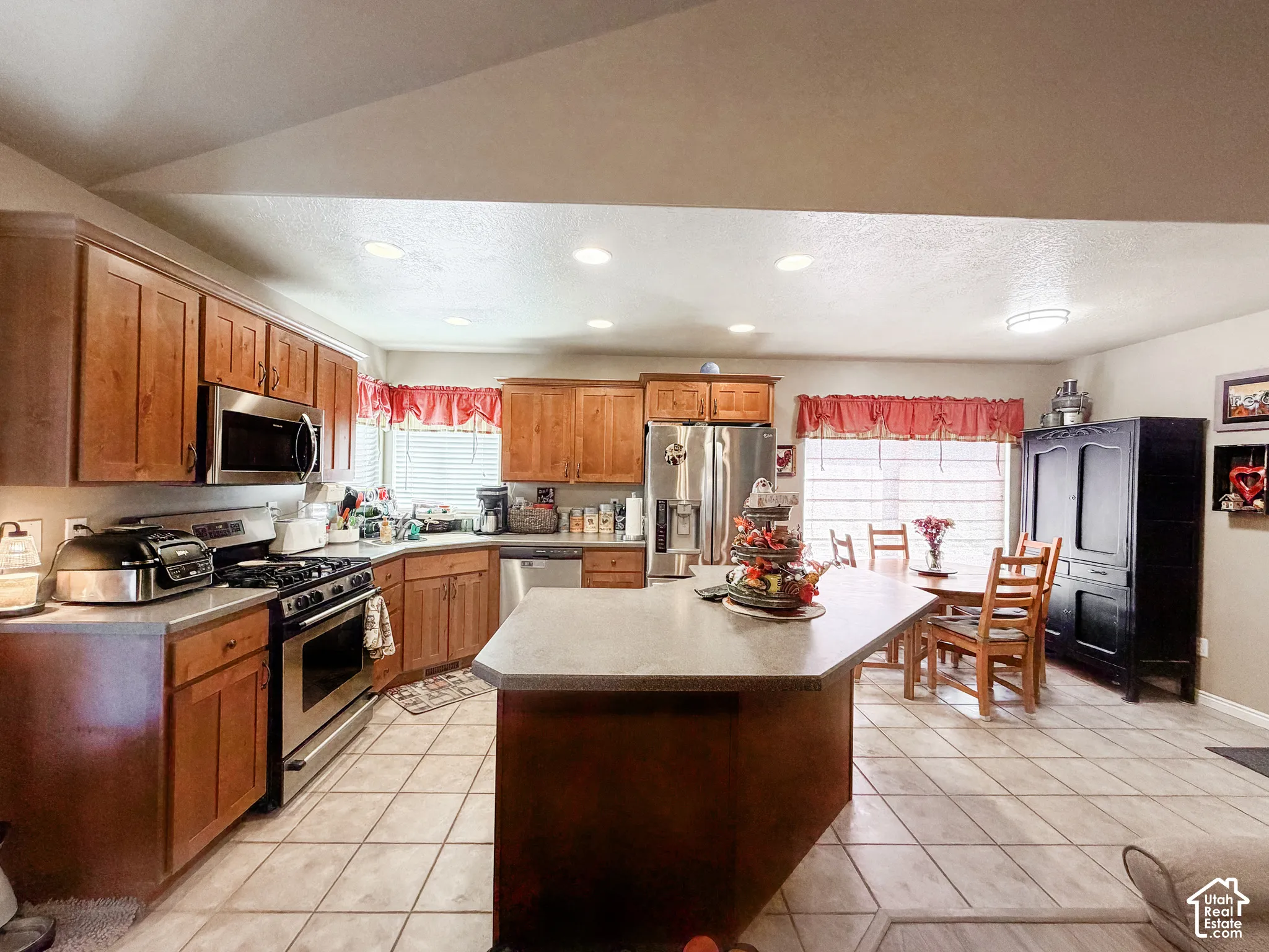 Kitchen featuring wood cabinetry, stainless steel appliances, a center island with countertop seating, and tile flooring