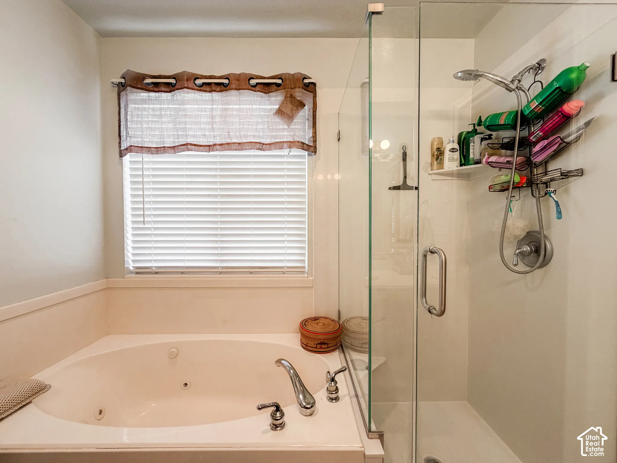 Soaking tub with deck-mounted chrome fixtures, adjacent to a glass-enclosed shower with a handheld shower head and an integrated shelf