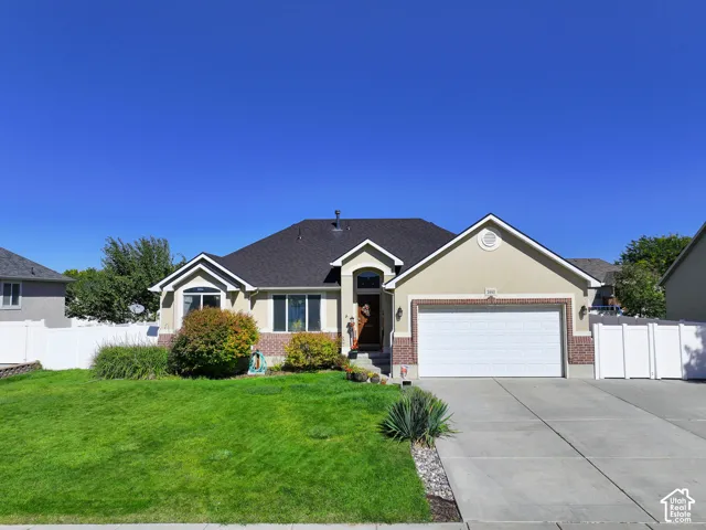 Stucco exterior with brick accents, attached two-car garage, concrete driveway, and a white vinyl fence
