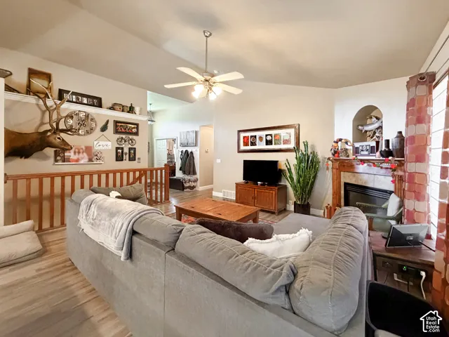 Vaulted ceiling with ceiling fan, wood-finish flooring, built-in fireplace, staircase with wood railing, and window with curtains