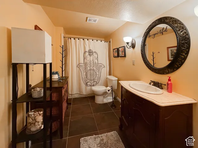 Bathroom with dark tile flooring, a single vanity with a light-colored countertop and undermount sink, and a commode