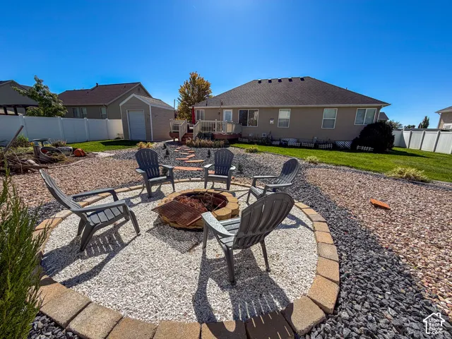 Backyard with a stone-edged fire pit area, gravel and rock landscaping, manicured lawn, and a shed structure