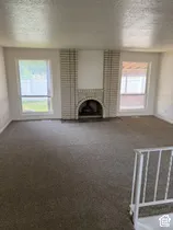 Spacious room featuring a brick fireplace with an arched opening, carpeted flooring, and multiple windows