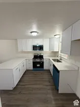 U-shaped kitchen with white cabinetry, light-toned countertops, wood-finish flooring, stainless steel sink, and built-in microwave