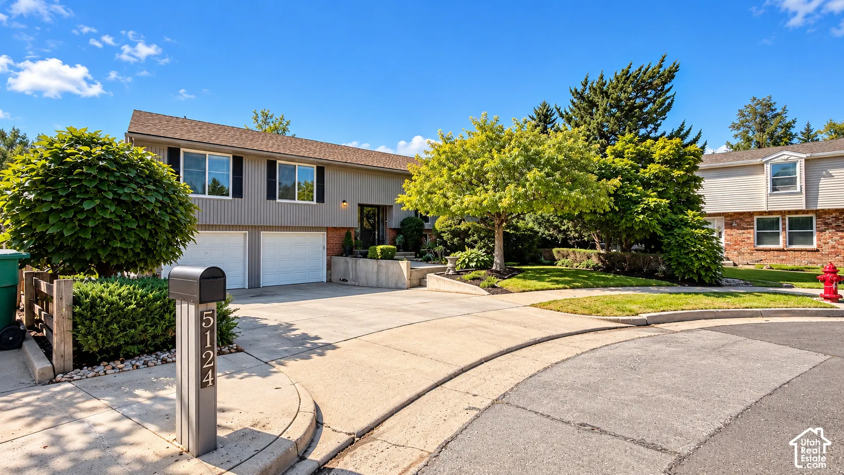 Split-level exterior with a two-car garage, mature landscaping, and a paved driveway