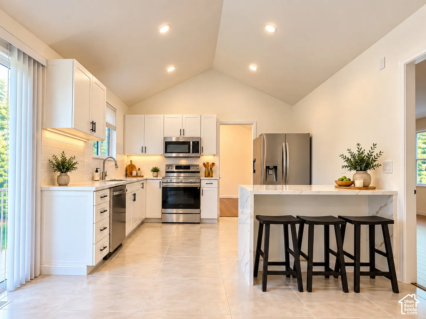 Kitchen featuring vaulted ceilings, recessed lighting, white cabinetry with dark hardware, stainless steel appliances, and a waterfall-edge island