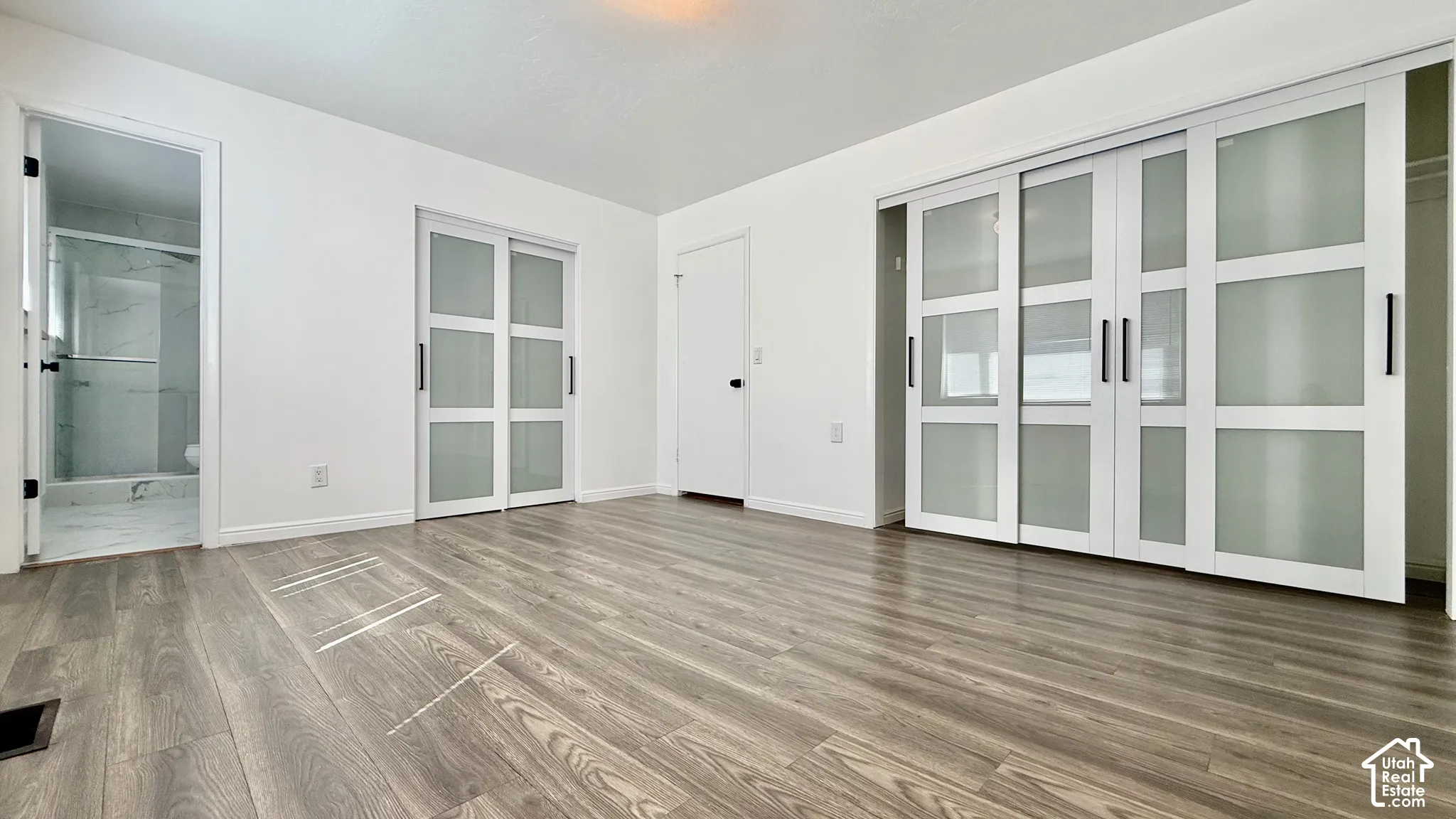 Wood-finish flooring throughout, white walls, two sets of sliding frosted glass doors, and a bathroom with a glass-enclosed shower