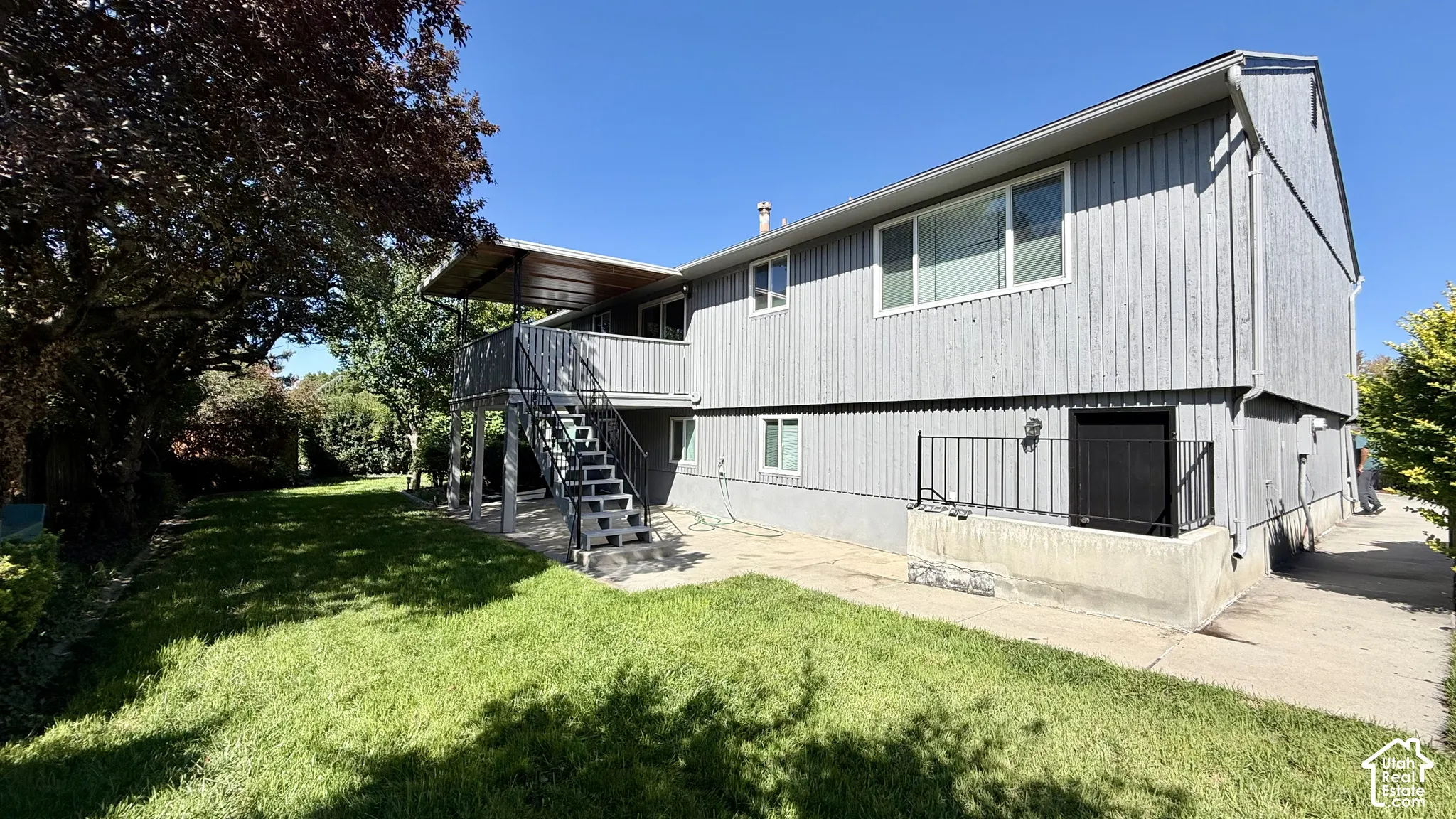 Expansive lawn with mature trees, multi-level deck, covered patio, exterior lighting, and a paved walkway