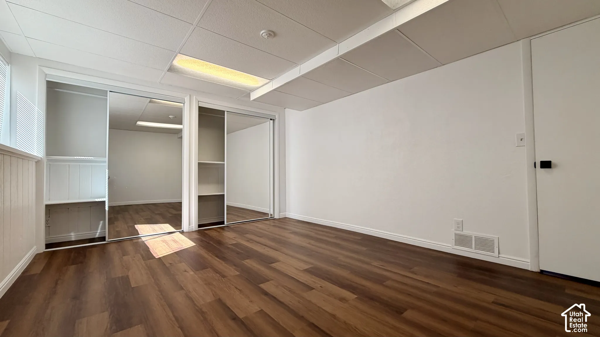 Wood-finish flooring, drop ceiling with recessed lighting, mirrored sliding closet doors with built-in shelving, white walls, and a white interior door
