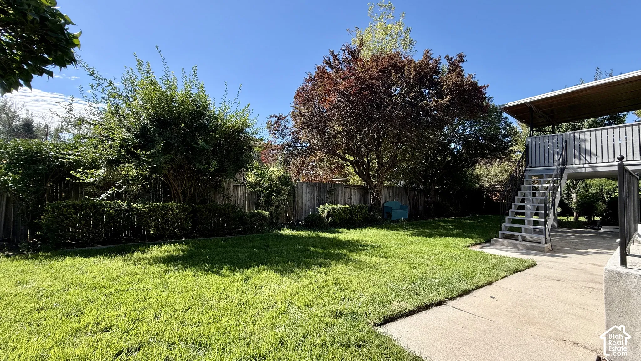 Expansive green lawn, mature trees, privacy fencing, concrete patio, and exterior staircase