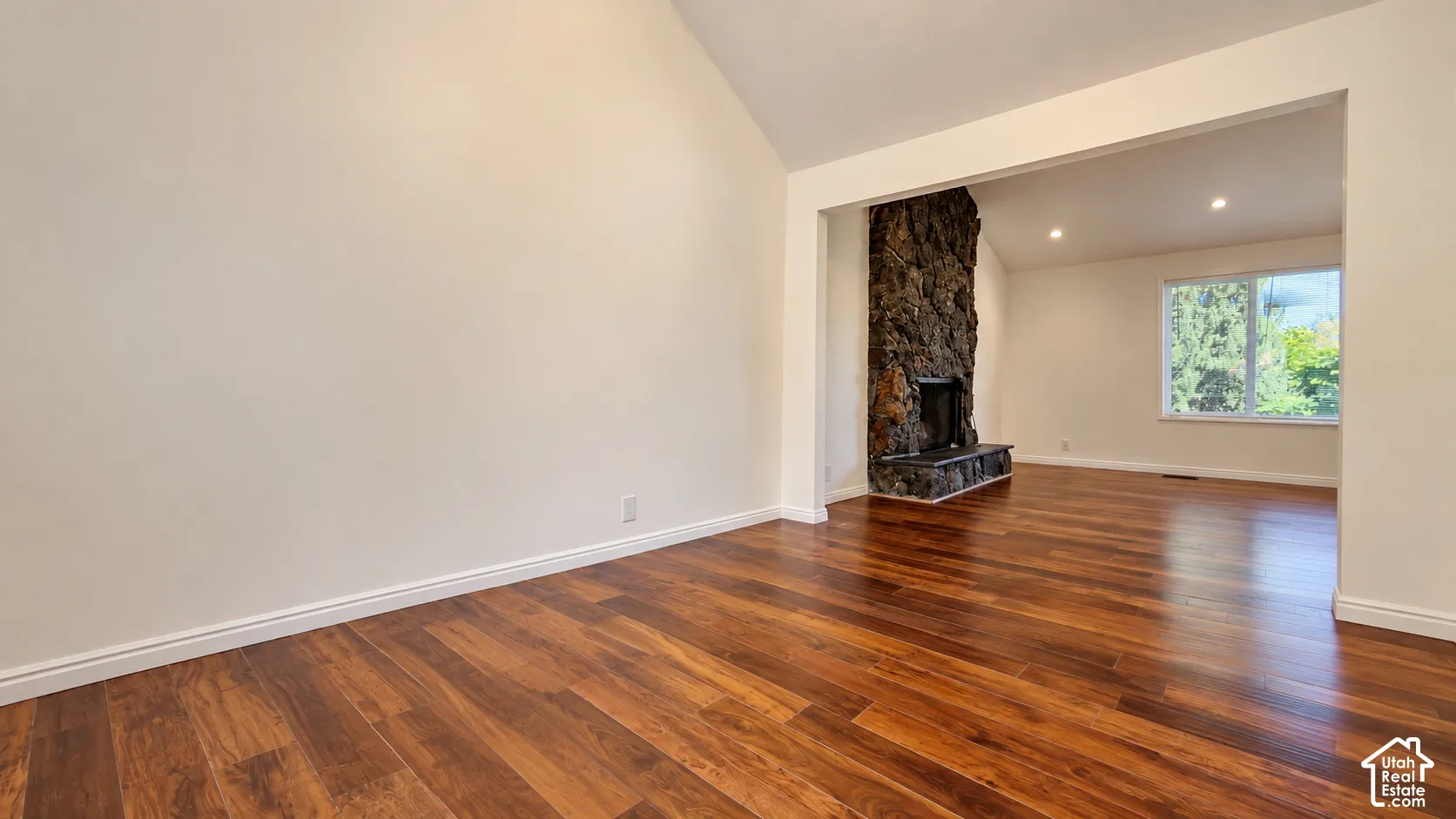 Vaulted ceiling, wood-finish flooring, stone fireplace, recessed lighting, and large windows