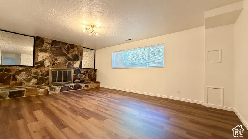 Spacious room featuring wood-finish flooring, a stone-clad fireplace with a metal insert, a horizontal window, and a ceiling-mounted lighting fixture