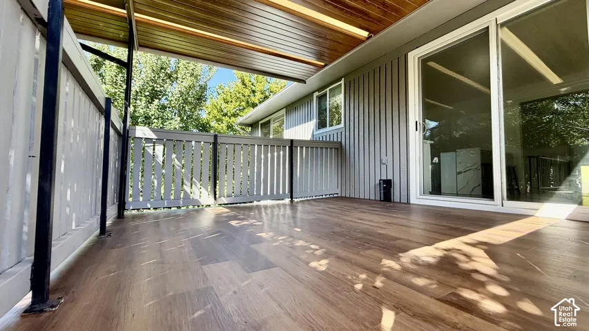 Covered balcony featuring wood-finish flooring, a white railing, and sliding glass doors