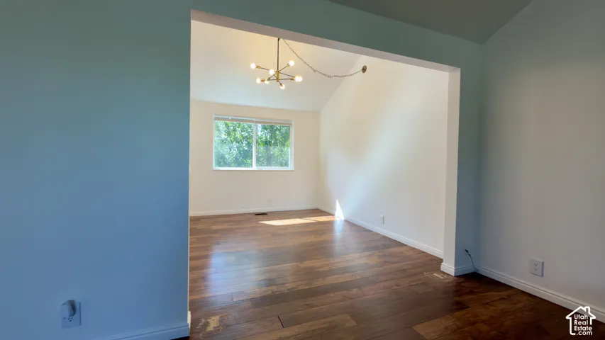Vaulted ceiling, modern sputnik chandelier, wood-finish flooring, white walls, and a large window
