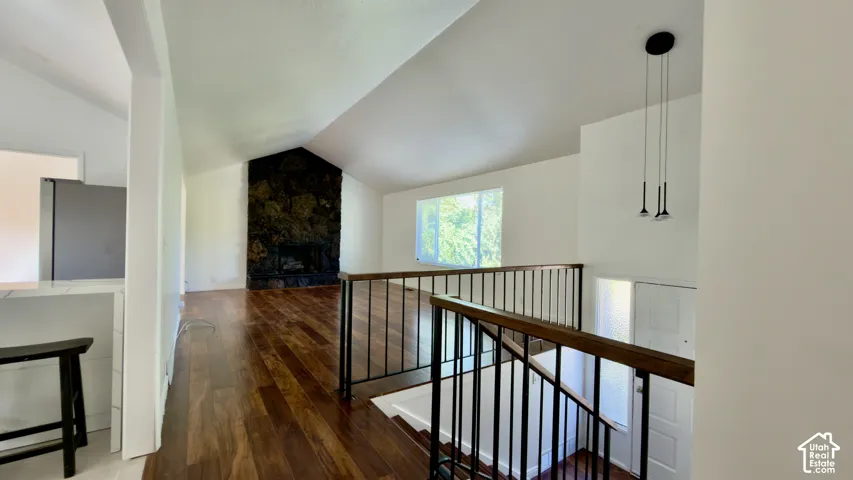 Vaulted ceiling, hardwood flooring, stone-clad fireplace, contemporary pendant light fixtures, and white walls
