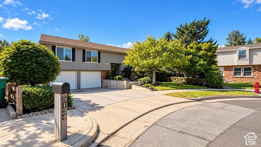 Split-level exterior with a two-car garage, mature landscaping, and a paved driveway