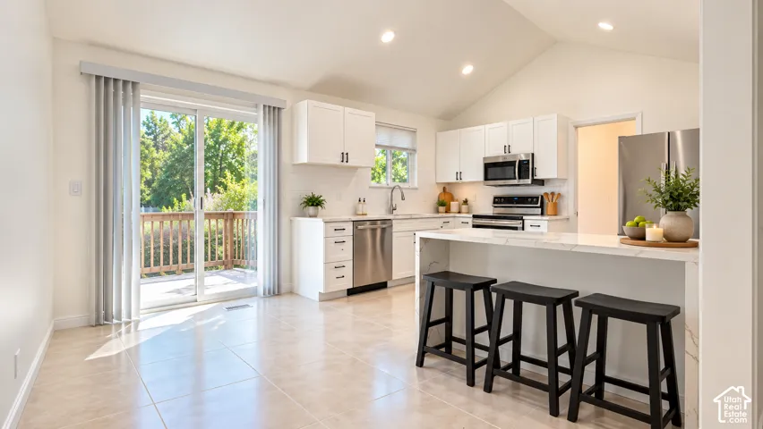Open-concept kitchen with vaulted ceilings, recessed lighting, white cabinetry, stainless steel appliances, and a counter-height island with a stone-finish surface
