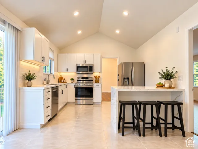 Kitchen featuring vaulted ceilings, recessed lighting, white cabinetry with dark hardware, stainless steel appliances, and a waterfall-edge island