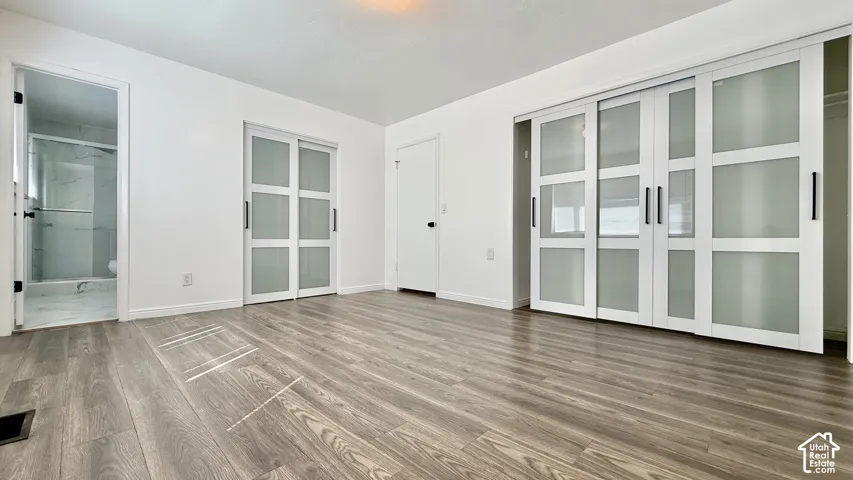 Wood-finish flooring throughout, white walls, two sets of sliding frosted glass doors, and a bathroom with a glass-enclosed shower