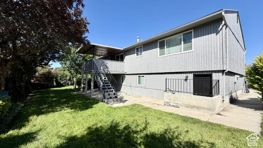 Expansive lawn with mature trees, multi-level deck, covered patio, exterior lighting, and a paved walkway