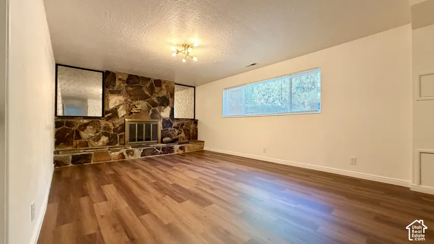Wood-finish flooring, stone fireplace with metal screen, built-in shelving, flush-mounted lighting, and a horizontal window