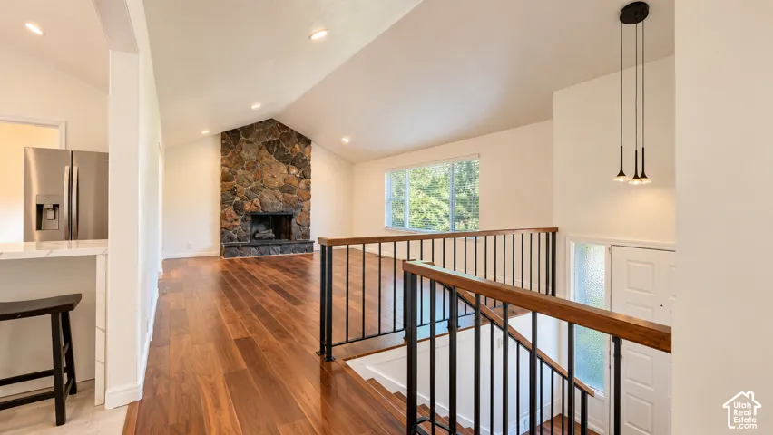 Vaulted ceiling with recessed lighting, wood-finish flooring, stone-clad fireplace, and stainless steel French door refrigerator